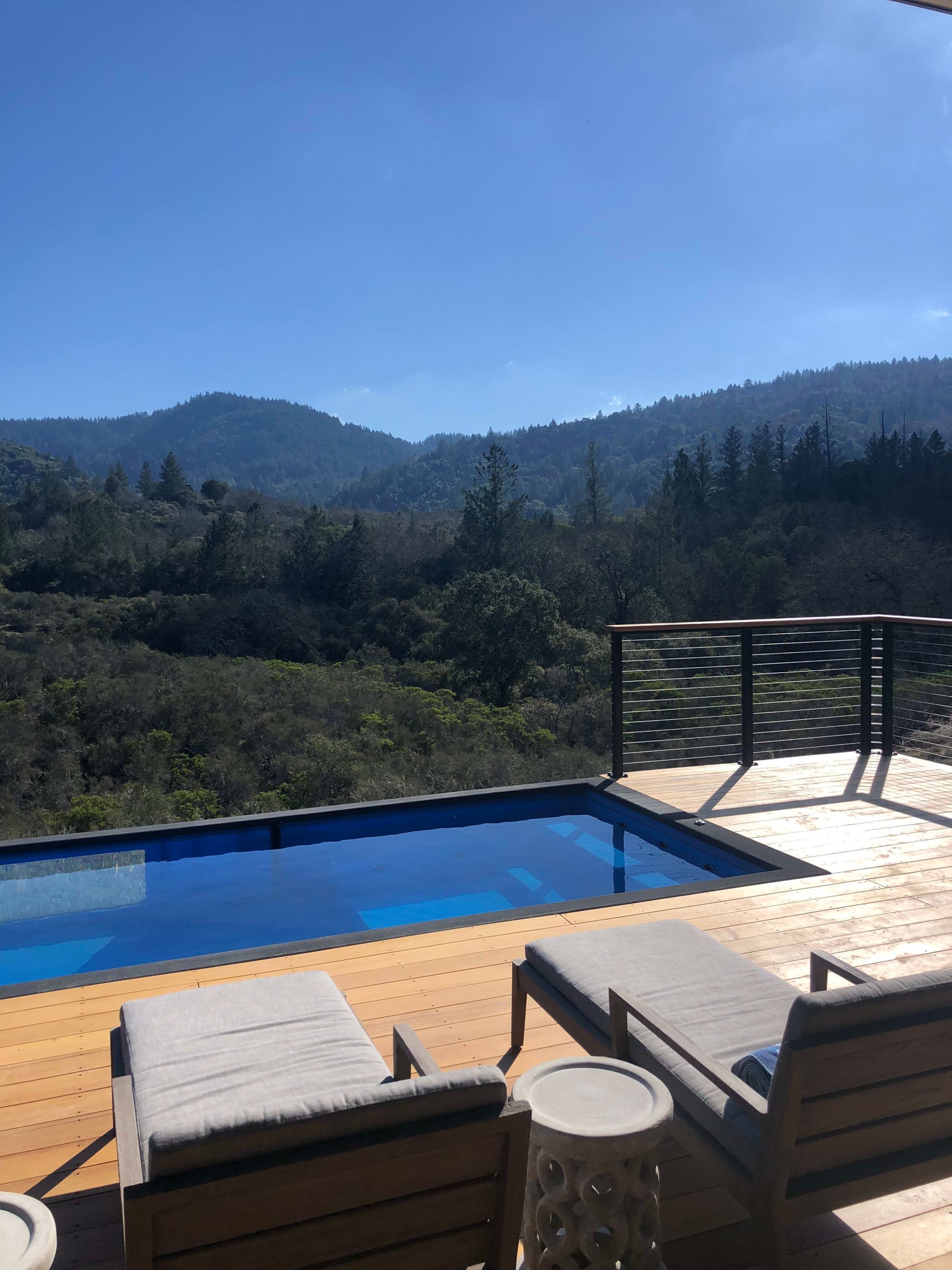 A poolside area with lounge chairs and a hot tub, overlooking a forested hillside.