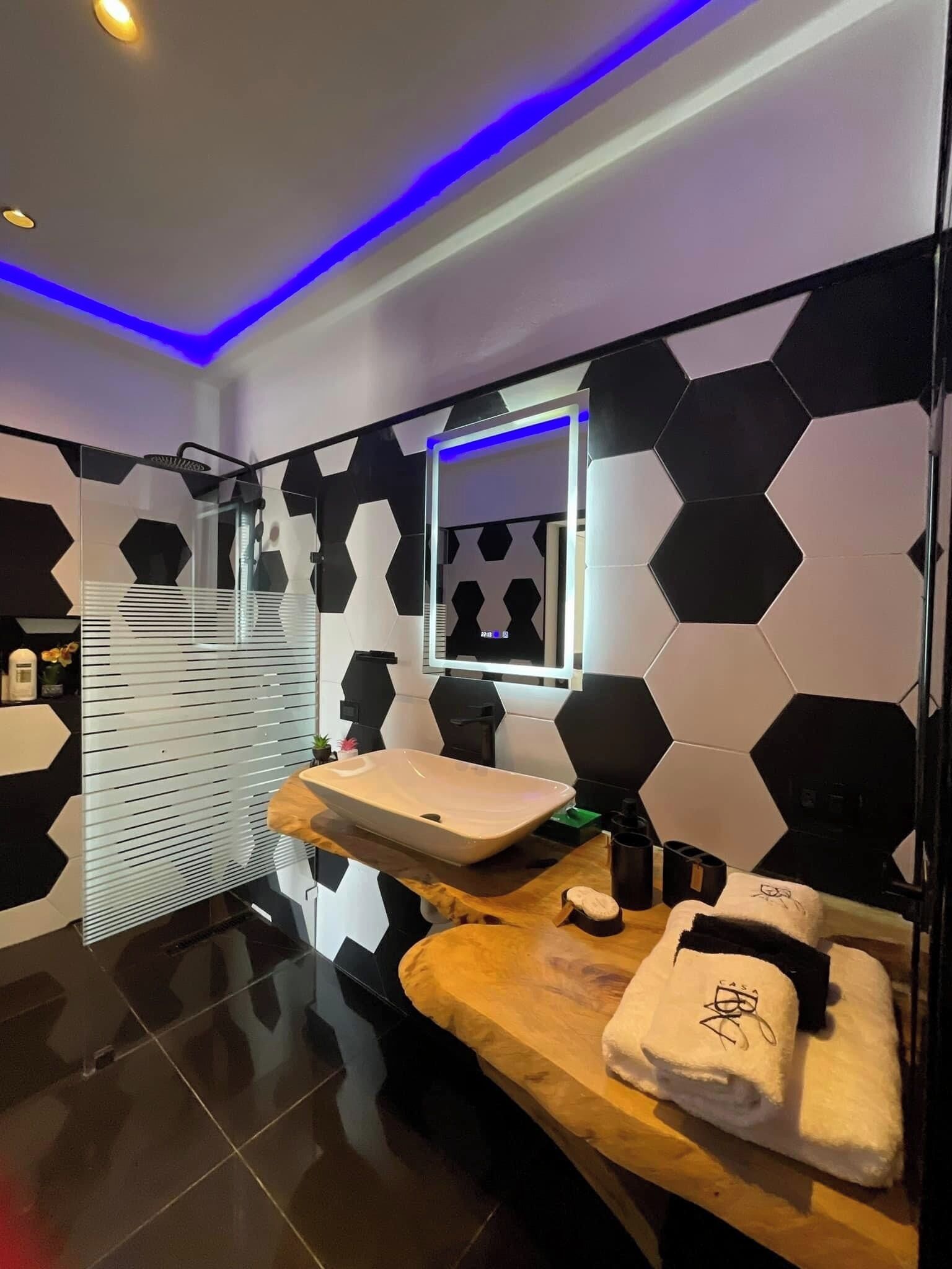 A modern bathroom with black and white hexagonal tiles, two sinks, a mirror, and a shower with a glass enclosure.