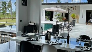 A modern dining area with a glass table, black and white chairs, and a view of a pool and palm trees outside. - Casa Black and White. Vista al Mar  (Las Galeras)
