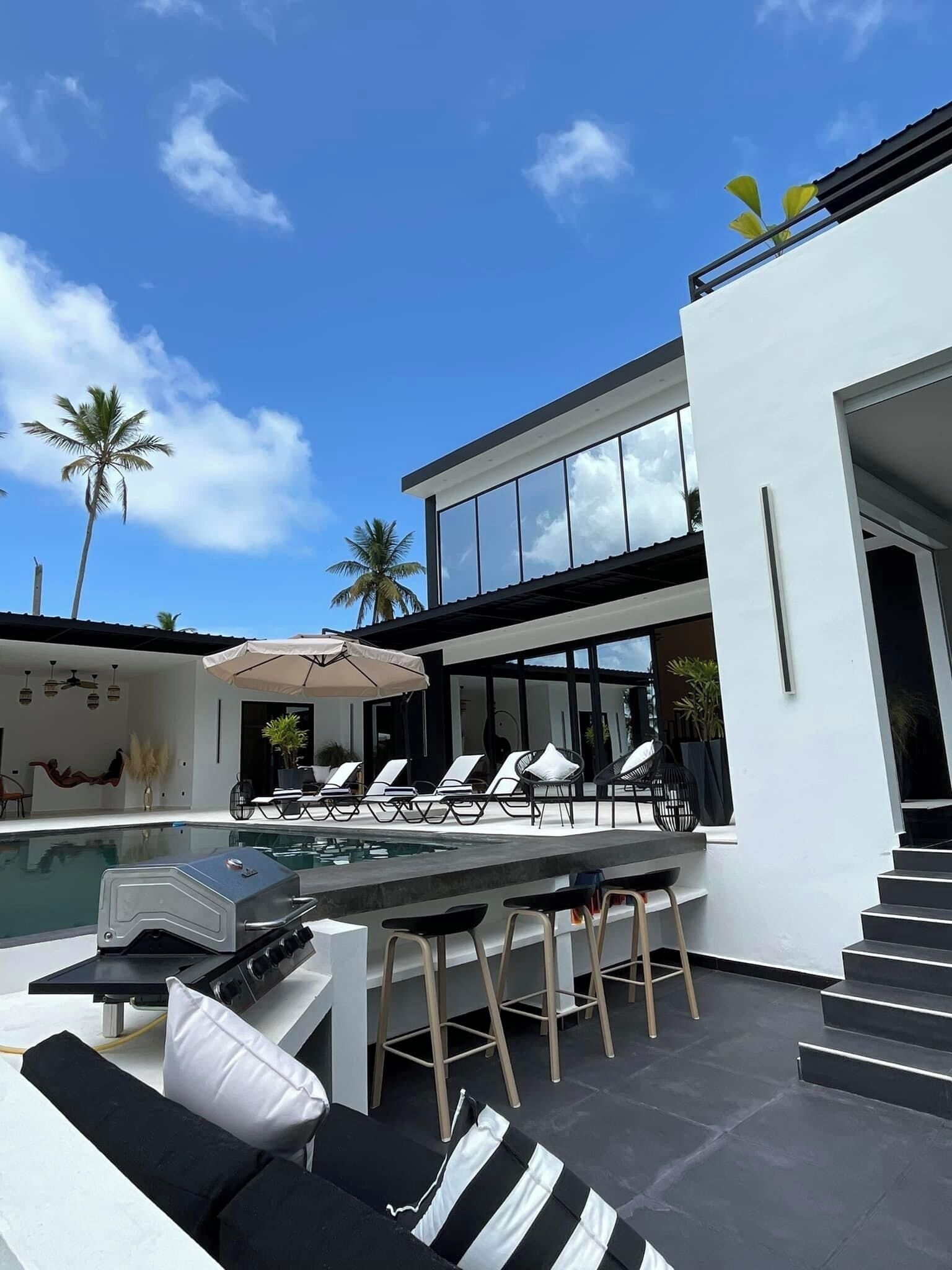 A modern outdoor pool area with lounge chairs and a barbecue grill.