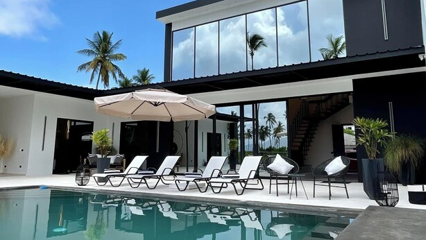A modern house with a pool, lounge chairs, and palm trees. - Casa Black and White. Vista al Mar  (Las Galeras)