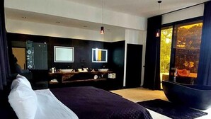 A modern bedroom with a large bed, a ceiling fan, a bathroom with a bathtub, and a view of a sunset through a window. - Casa Black and White. Vista al Mar  (Las Galeras)