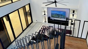 A modern living room with a large TV, a staircase, and a view of palm trees through large windows. - Casa Black and White. Vista al Mar  (Las Galeras)