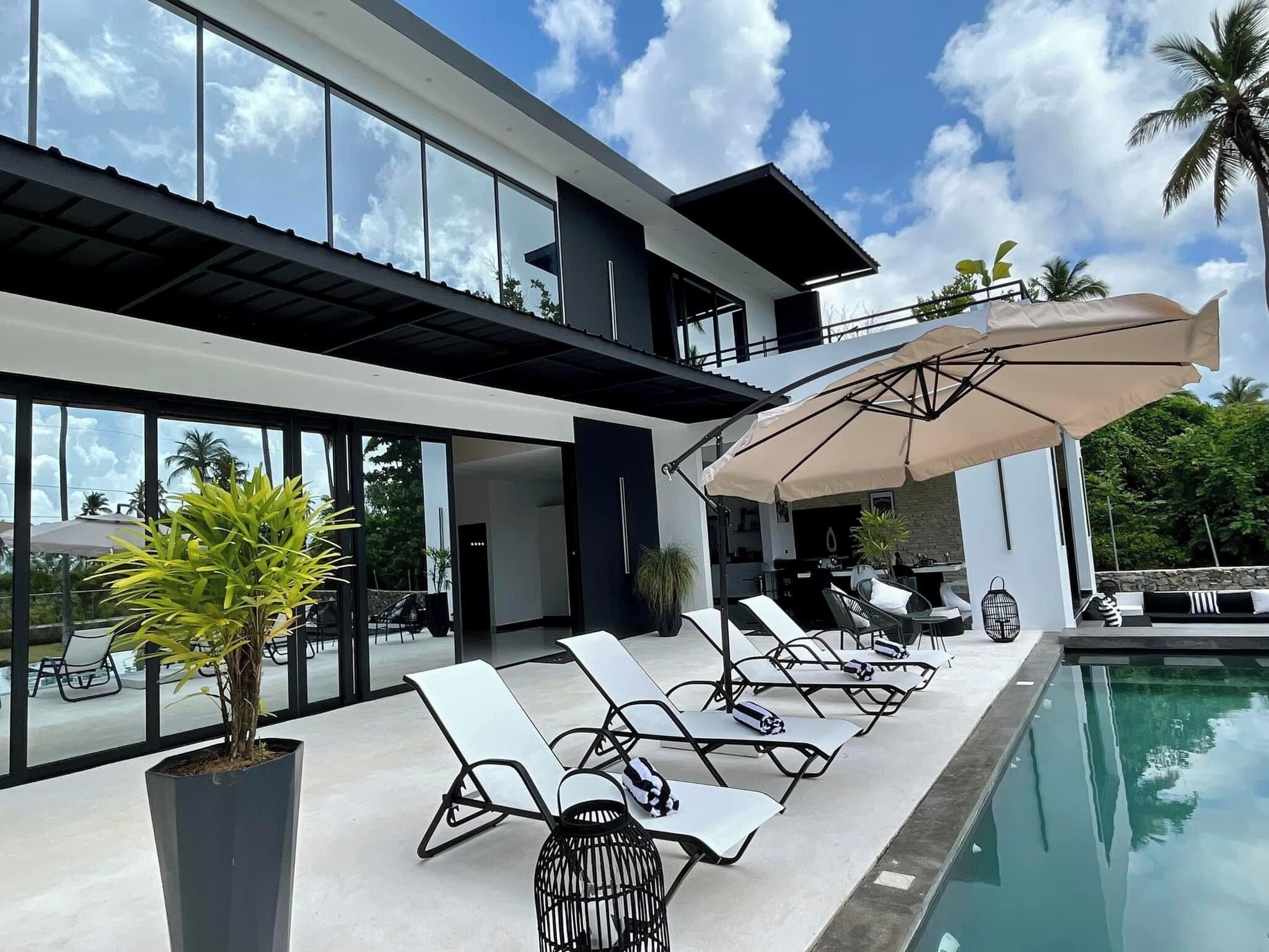 Une maison moderne avec une piscine, des chaises longues et des parasols.