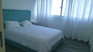 A bedroom with a bed, a nightstand, and a window with curtains. - Baya Azul Bayahibe - Penthouse 402 (San Rafael del Yuma)