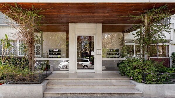 A modern building entrance with a wooden overhang, a car parked in the driveway, and a staircase leading to the entrance.