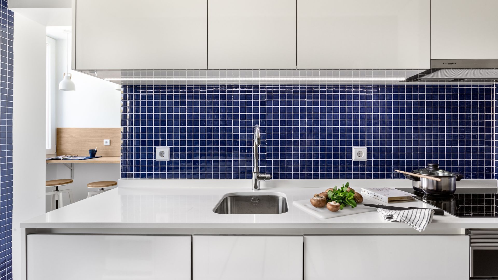 A modern kitchen with a white countertop, a stainless steel sink, and a blue-tiled backsplash.