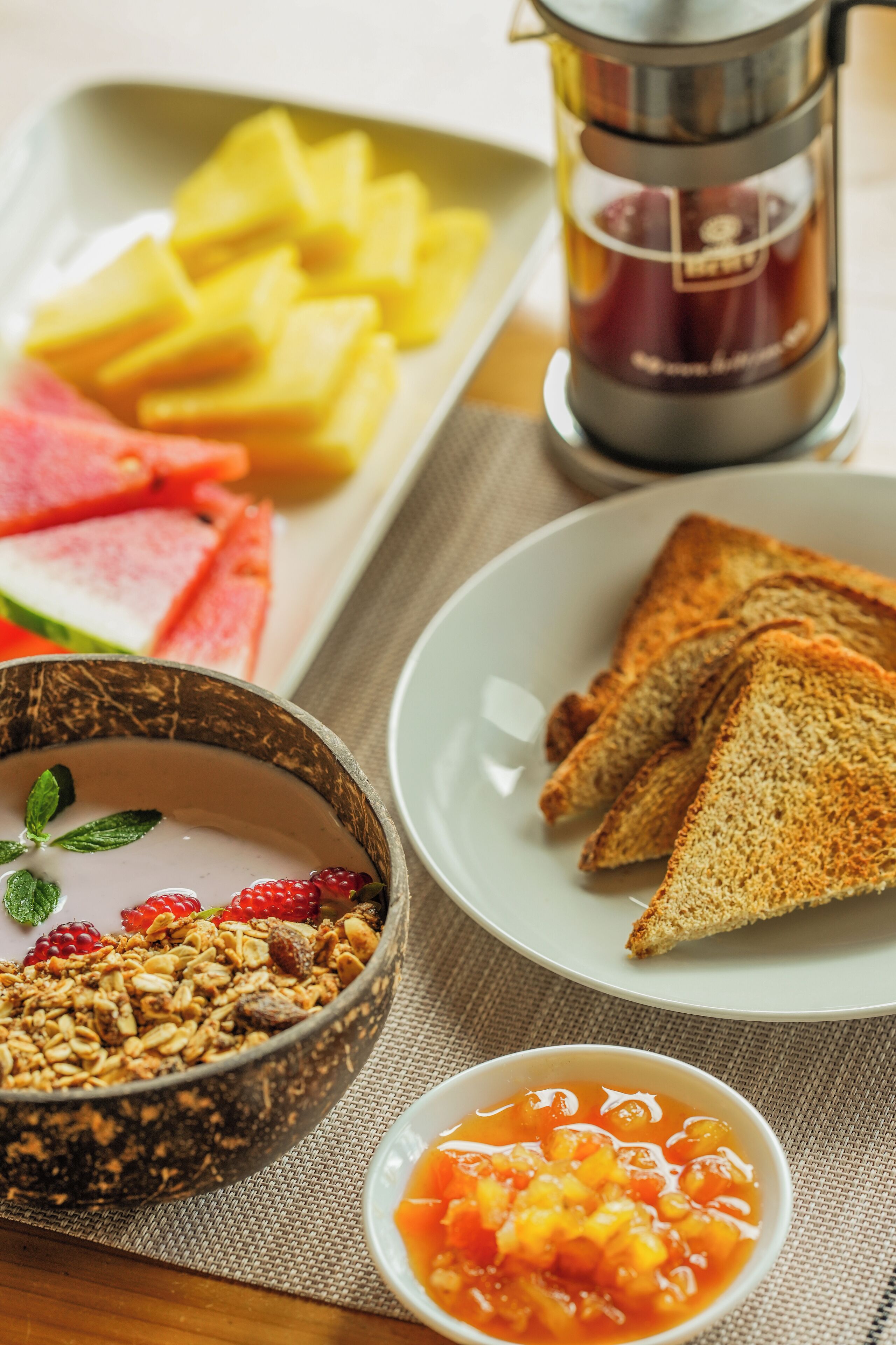 Desayuno con tostadas, un bol de granola y un recipiente pequeño de compota de frutas.
