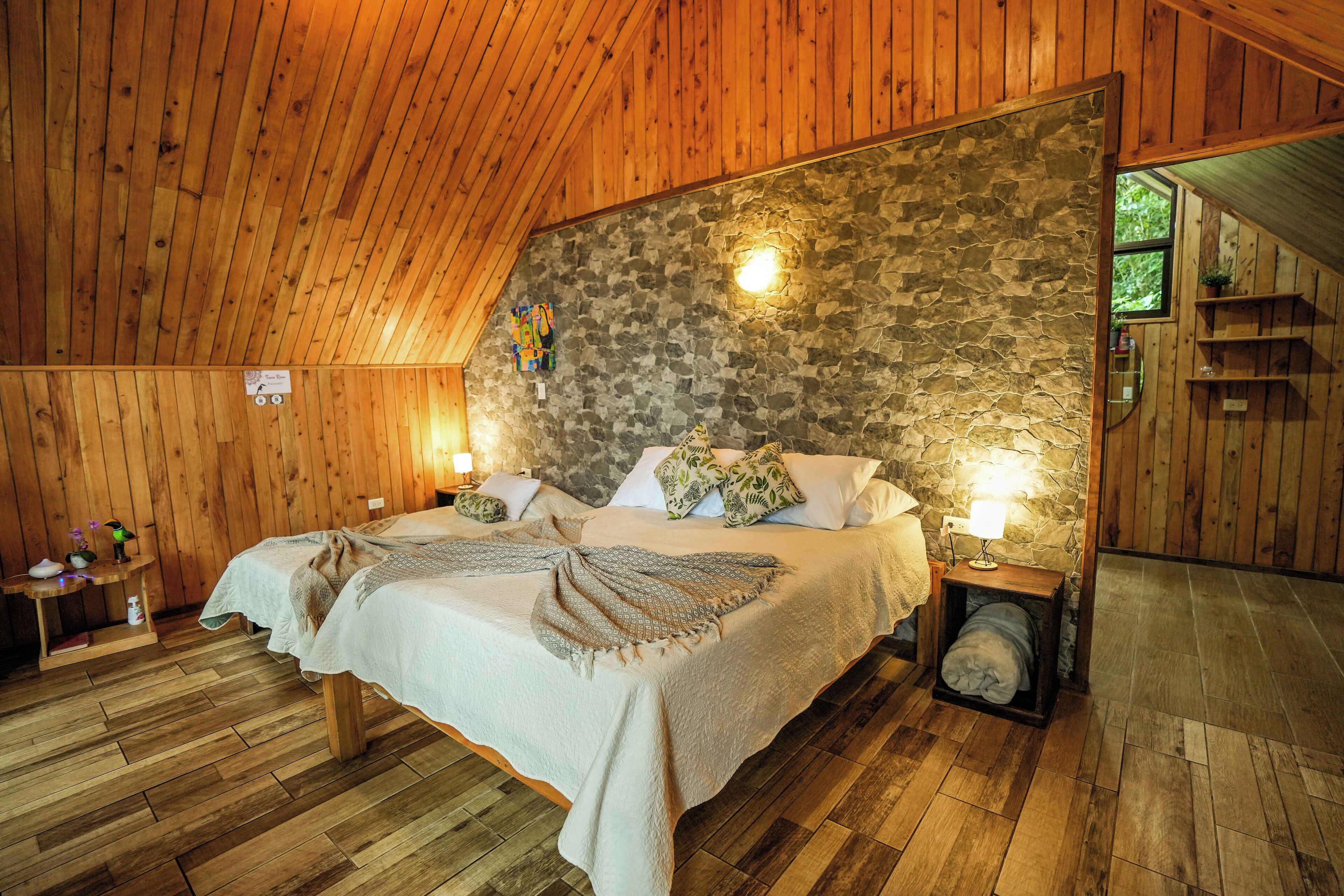 A cozy bedroom with a stone wall, wooden ceiling, and a bed with pillows and a blanket.