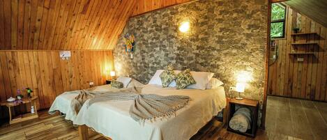 A cozy bedroom with a stone wall, wooden ceiling, and a bed with pillows and a blanket.