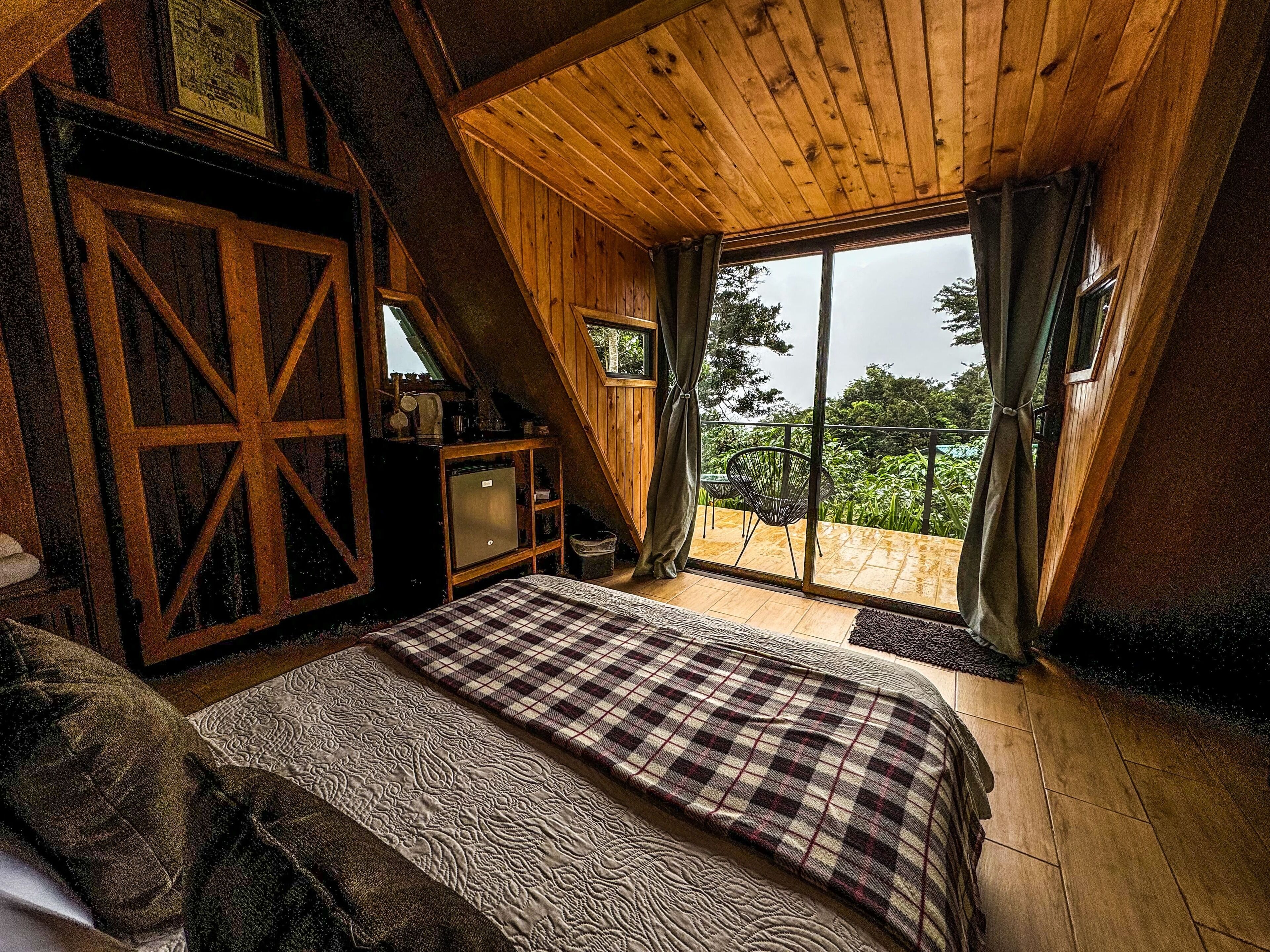 Un dormitorio acogedor con una cama grande, un escritorio de madera y un balcón con vistas a zonas verdes.