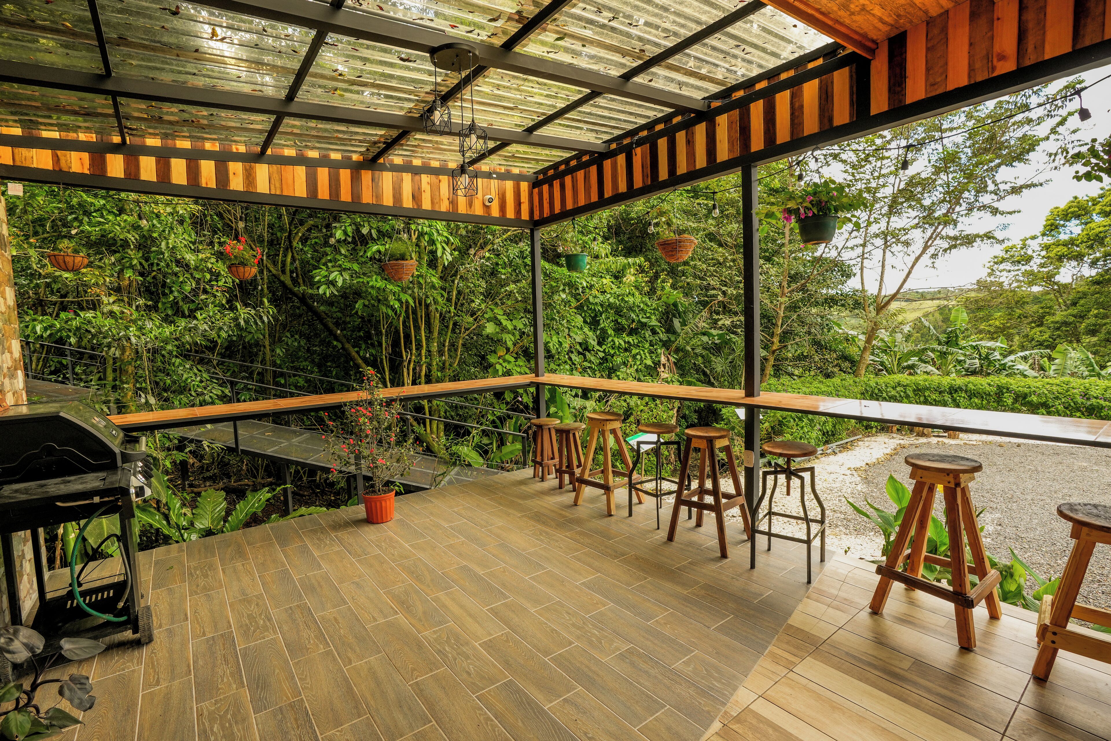 An outdoor patio with wooden flooring, a grill, and bar stools.