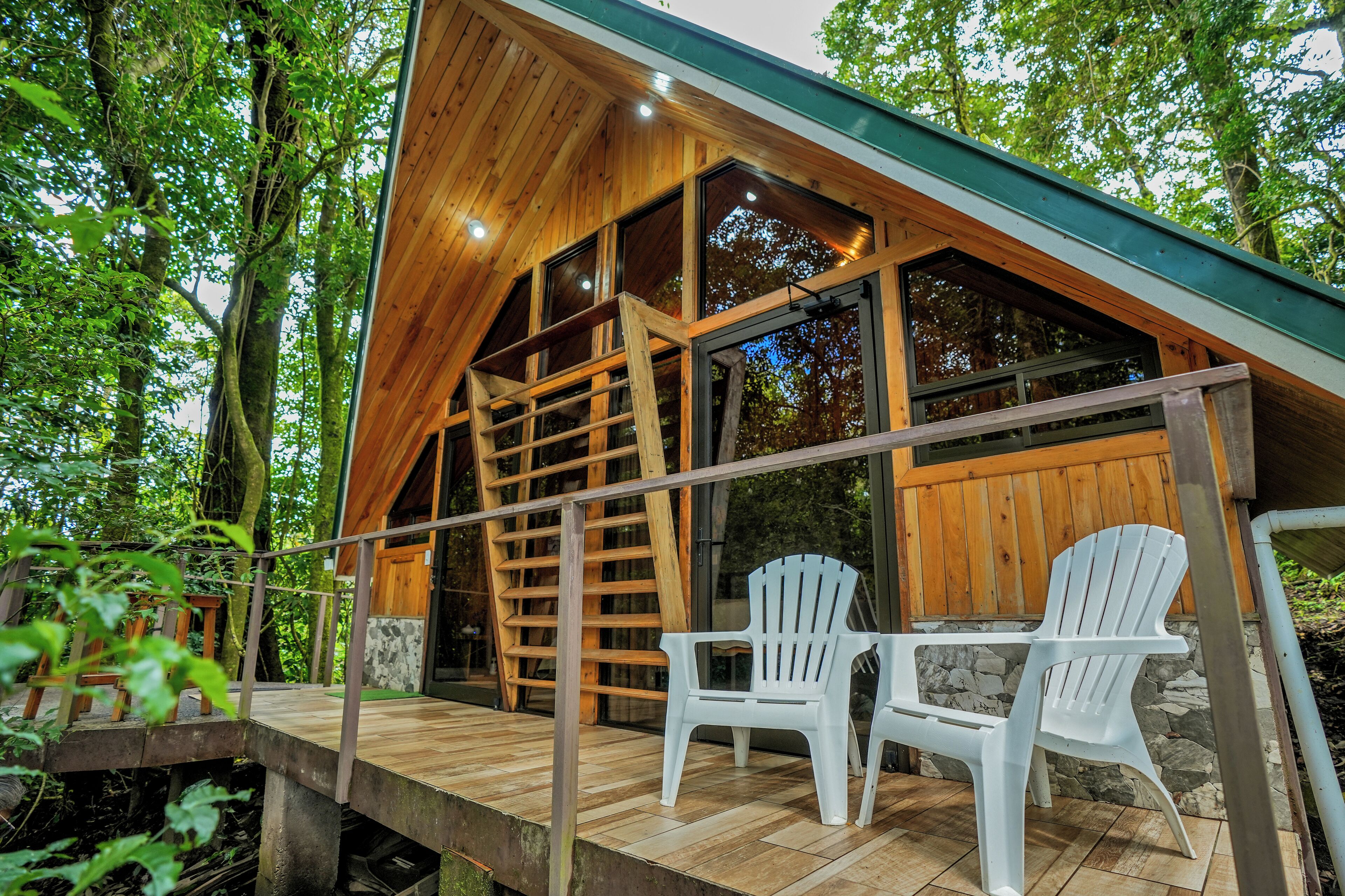 A wooden cabin with a sloped roof, a wooden deck, and two white plastic chairs.