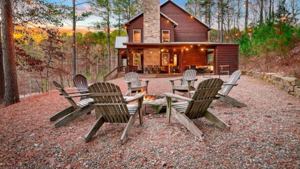 Eine rustikale Holzhütte mit einem Steinkamin, einer Holzterrasse und Adirondack-Stühlen um ein Feuerbecken.