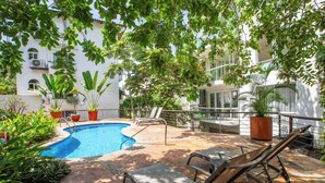 A pool area with lounge chairs, potted plants, and a building in the background. - Peaceful Oasis in Romantic Zone w/ Pool & Parking (Puerto Vallarta)
