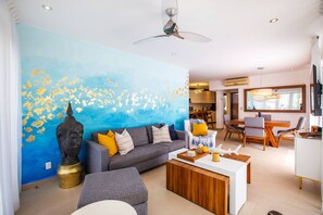 Una sala moderna con un mural azul en la pared, un sofá, una mesa de centro y una zona de comedor con sillas y una mesa.