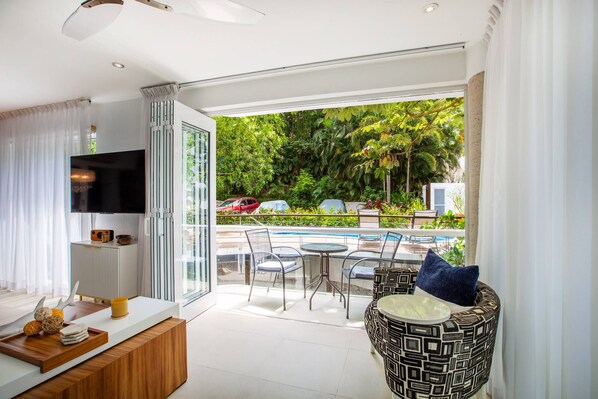 Una sala de estar moderna con televisor, un comedor con una silla estampada y vistas a una piscina y vegetación afuera.