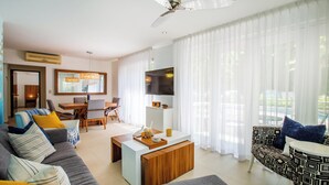 A modern living room with a sofa, coffee table, and patterned armchair. There is a dining area with a table and chairs, and a TV mounted on the wall. - Peaceful Oasis in Romantic Zone w/ Pool & Parking (Puerto Vallarta)