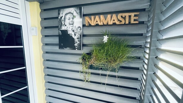 Una entrada moderna a un edificio con fachada gris, una fotografía montada y el nombre 'NAMASTE' exhibido con gran destaque.