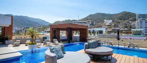 Zona de piscina en la azotea con sillones de descanso y terraza de madera.
