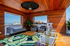 Ein modernes Interieur mit Deckenventilator, Holzwänden, einer Couch, zwei Sesseln, einem Couchtisch und Blick auf die Stadt.