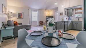 A modern living room with a dining area, grey furniture, a ceiling fan, and a kitchen with grey cabinets and a window. - No Cleaning Fee!!~King Bed~Near Dickies,TCU, cultural district~Sleeps 6 (Fort Worth)
