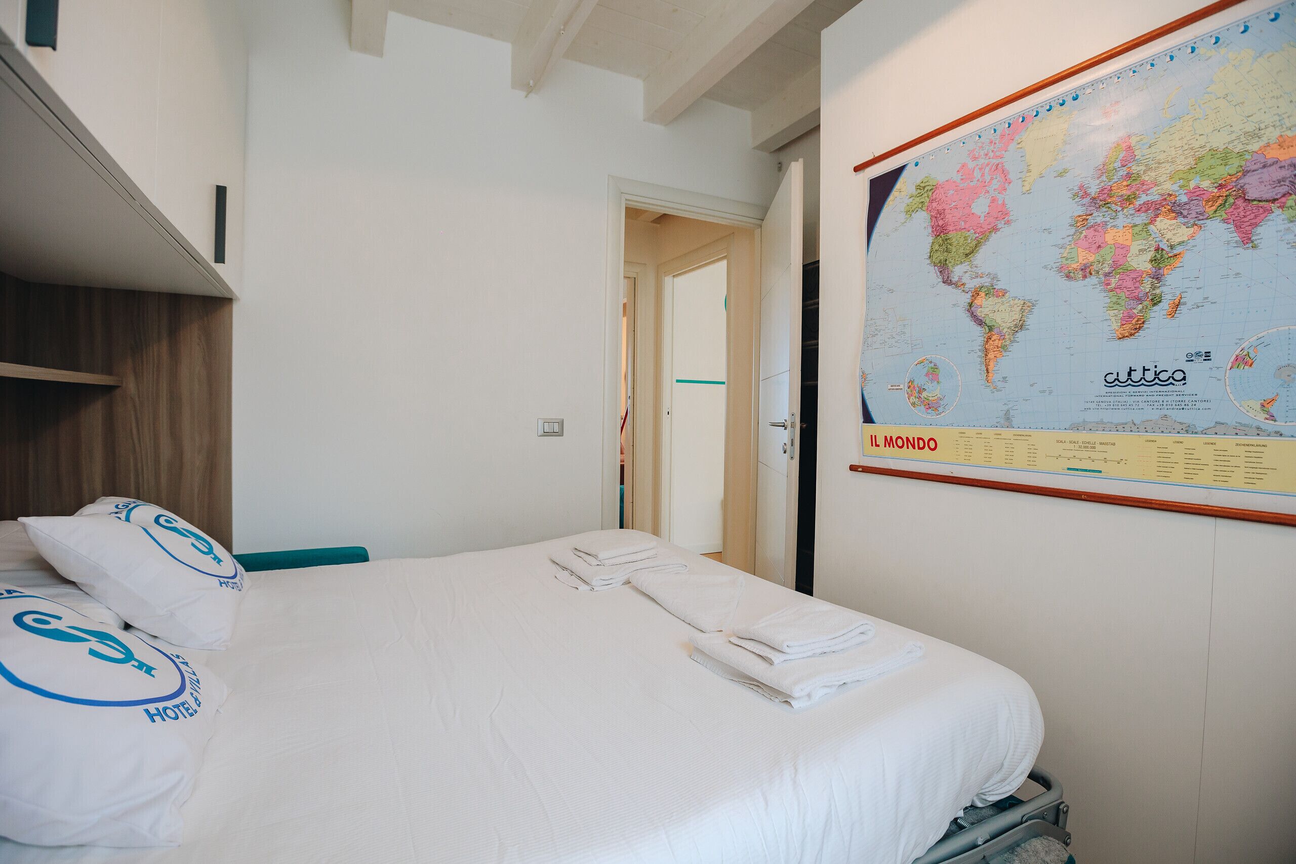 A hotel room with a bed, pillows, a map on the wall, and a door leading to another room.