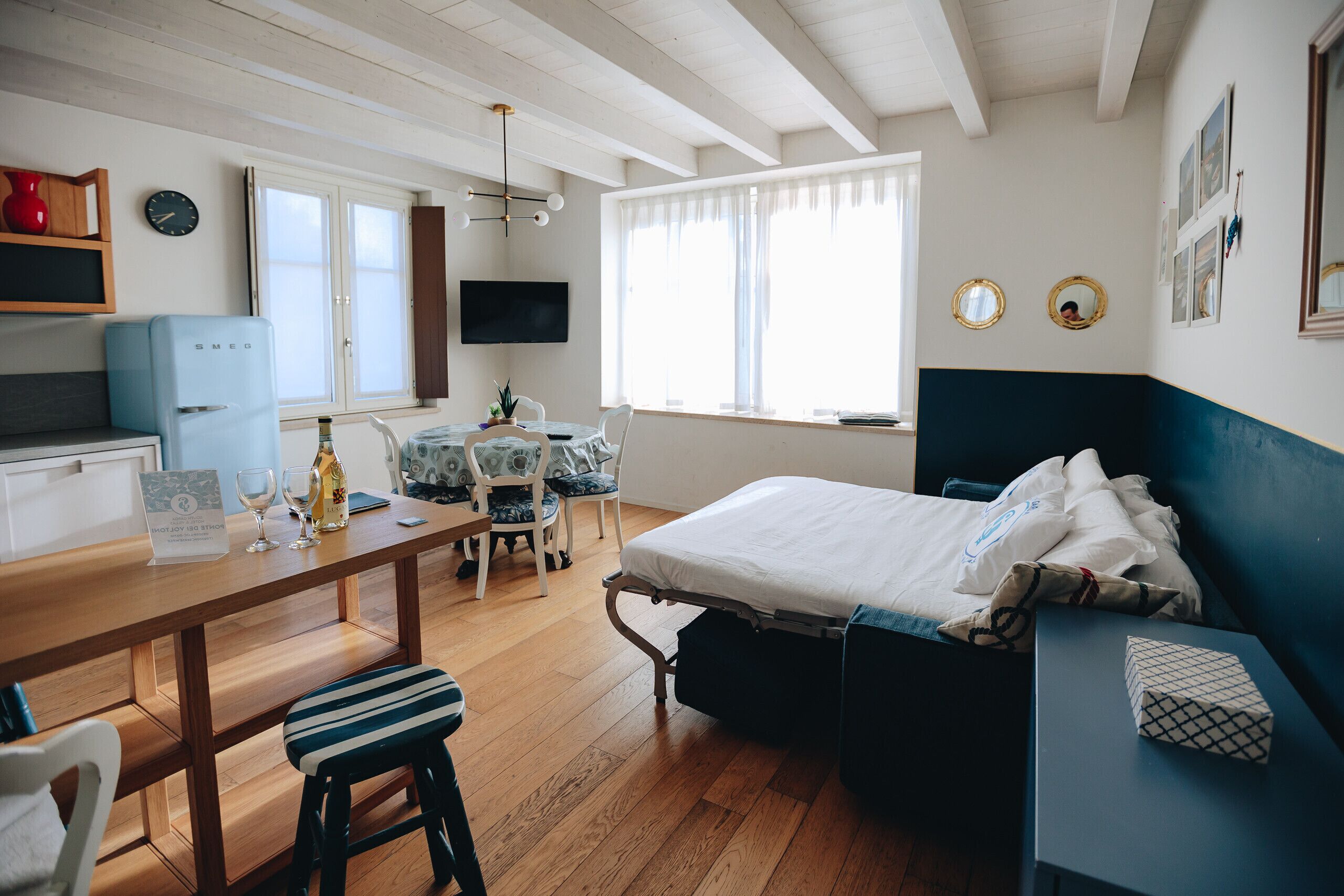 A room with a bed, a desk, a chair, a small table, a TV, and a window.