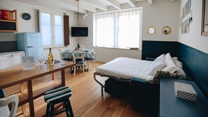 Una habitación con cama, escritorio, silla, mesita, televisor y ventana.