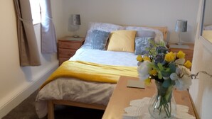Een slaapkamer met een bed, nachtkastjes, een dressoir, een vaas met bloemen en een aan de muur hangend schilderij.