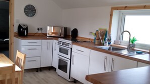 Een moderne keuken met witte kastjes, een houten aanrecht, een ingebouwde oven, een magnetron en een spoelbak.