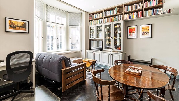 Un espace de bureau moderne doté d’une grande fenêtre, d’une bibliothèque et d’une table ronde en bois.