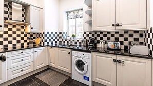 Une cuisine moderne avec des meubles blancs, un crédence à carreaux noirs et blancs, un lave-linge encastré et une fenêtre agrémentée de rideaux décoratifs.