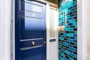 Eine blaue Tür mit einem Zahlenschloss, eine Wand mit blauen Fliesen und ein weißer Türrahmen.