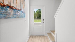 A hallway with a white door, a painting of sailboats on the wall, and a view of a green landscape through the door. - NEW! Townhome in Beautiful Santa Rosa Beach! (Santa Rosa Beach)