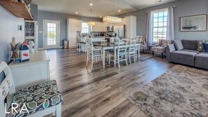 A spacious living area with a dining table, white chairs, a gray sofa, and a patterned rug. - Relax & Recharge at Paid Time Off (Surf City)