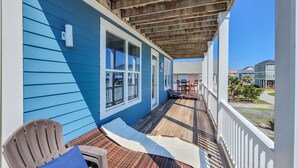 A covered porch with a blue exterior, wooden beams, and a view of neighboring houses. - Relax & Recharge at Paid Time Off (Surf City)