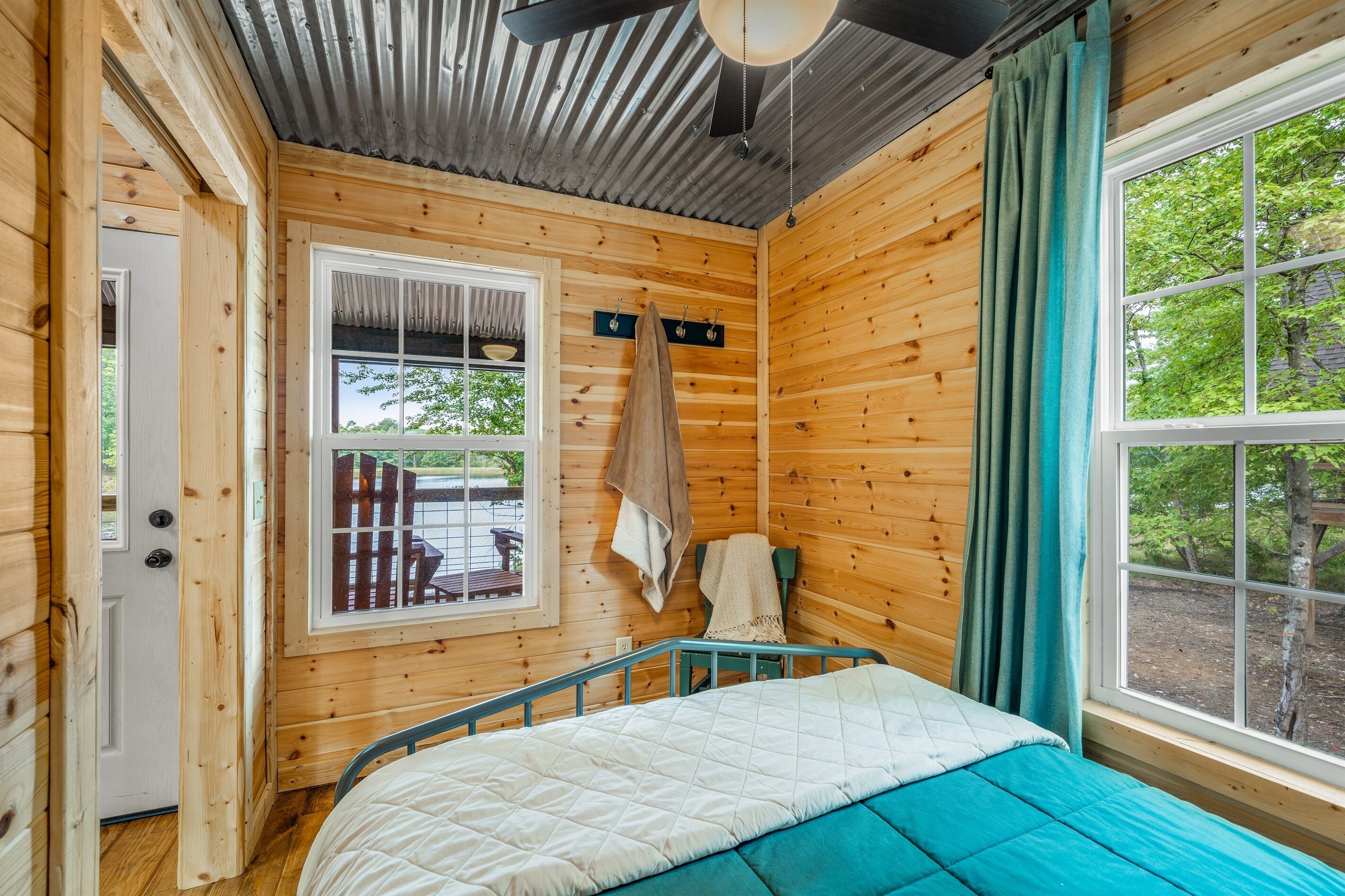 Ein Holzhütten-Zimmer mit Bett, einem Vorhangfenster, einer Tür und einem Deckenventilator.