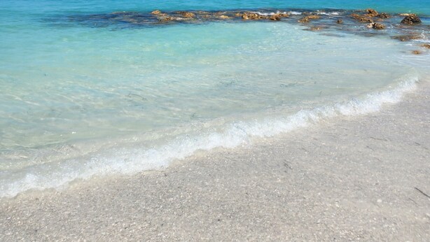 Une plage à l’eau turquoise et limpide, avec un rivage sablonneux et quelques rochers épars.