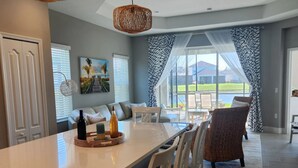 Une cuisine moderne dotée d’un grand îlot central, de luminaires suspendus et offrant une vue sur l’extérieur.