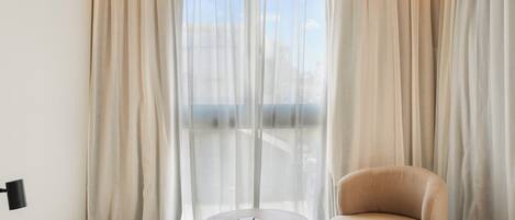 Una habitación moderna con una mesa redonda, un sillón beige y cortinas traslúcidas.