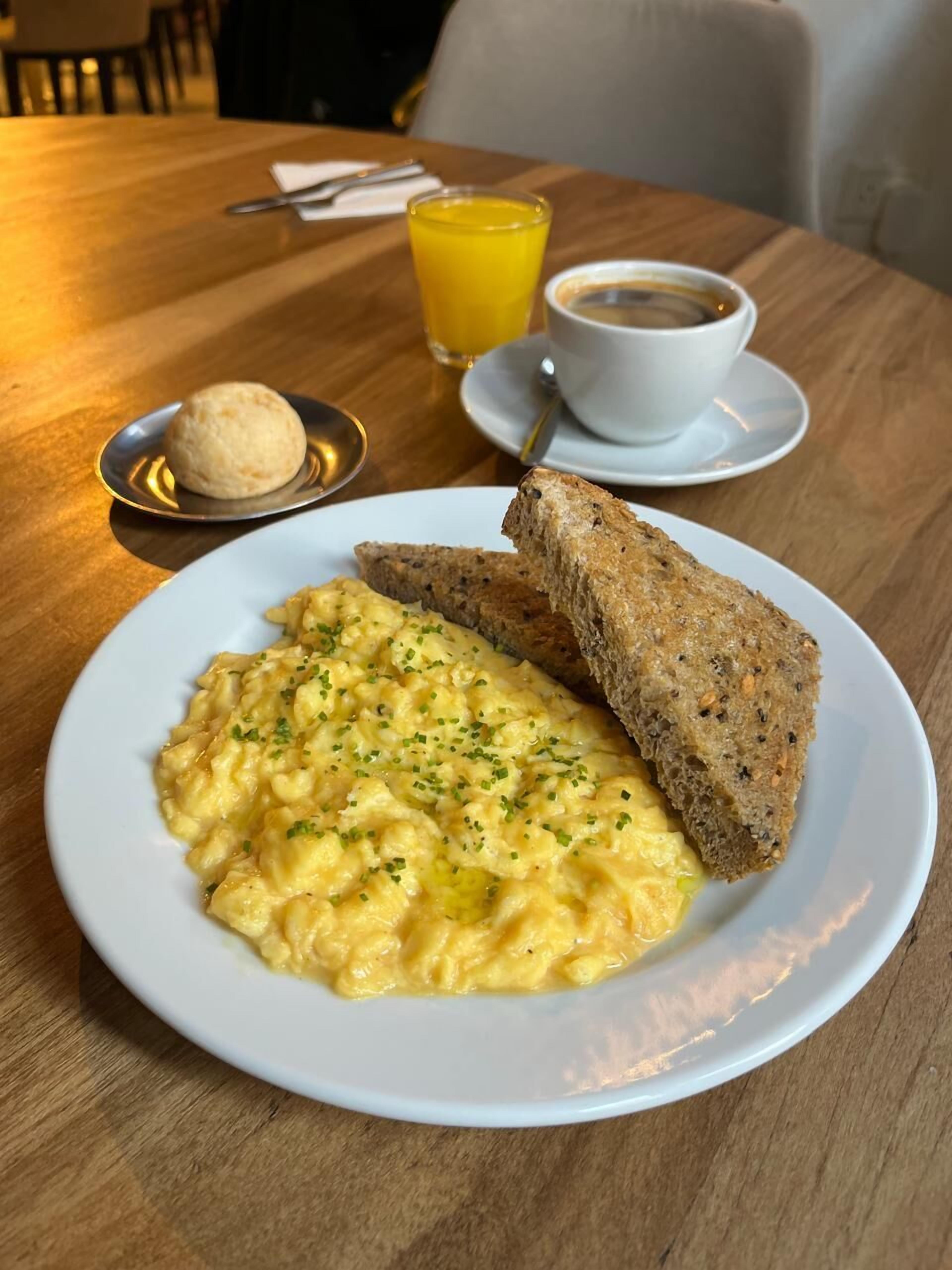 A breakfast plate with scrambled eggs, toast, and a cup of coffee on a wooden table.