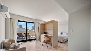 A modern hotel room with a large window, a desk, a chair, a bed, and a balcony with outdoor seating. - Vilon Recoleta Hotel (Buenos Aires)