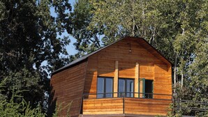 Una cabaña de madera con balcón, rodeada de árboles.