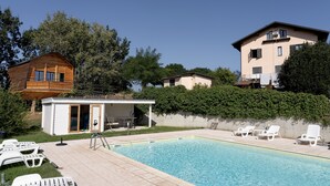 Una piscina con sillas de descanso, una cabaña de madera y un edificio de dos pisos con balcón.