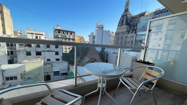 A balcony with a glass table and two chairs, overlooking a cityscape with various buildings. - Luxury and Comfort in San Telmo With Pool and Balcony (Buenos Aires)