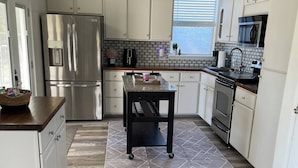 A modern kitchen with white cabinetry, stainless steel appliances, and a wooden floor.