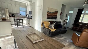 A modern living space with a wooden dining table, a leather sofa, and a kitchen area.