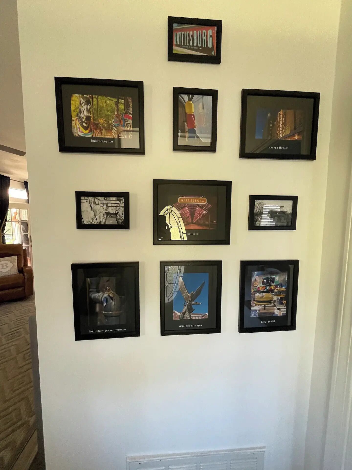 A wall with nine framed pictures, including a Hollisterburg sign, a pocket watch, and a statue of an eagle.