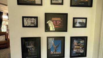 A wall with nine framed pictures, including a Hollisterburg sign, a pocket watch, and a statue of an eagle.